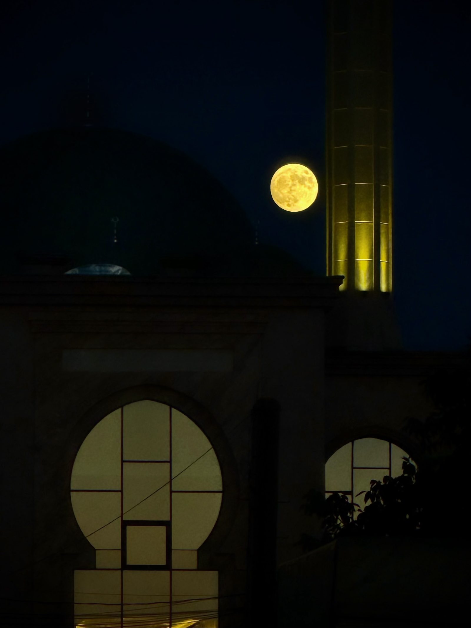 Full Moon Beside a Lit Tower at Night