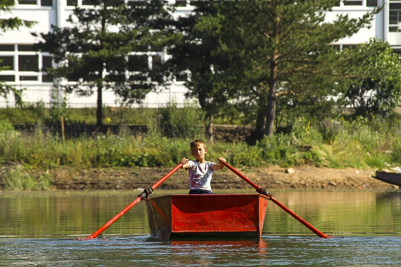 Boy Rowing a Red Boat on a Pond