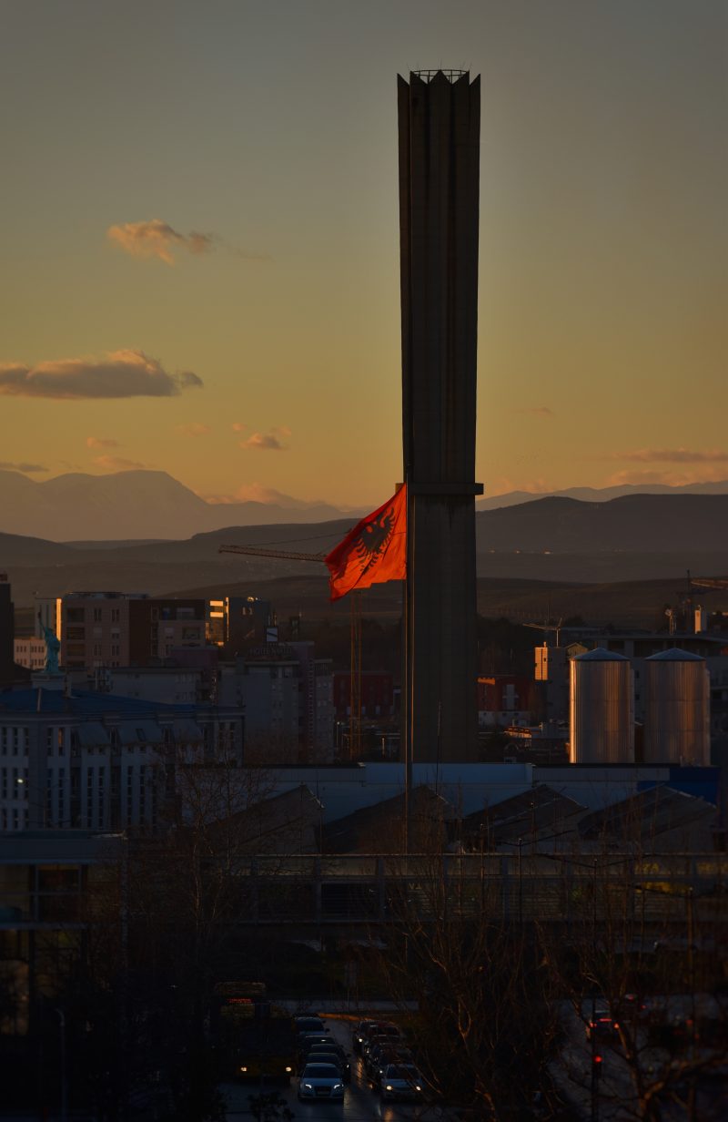 Tall Chimney and Red Flag Over a City at Dusk